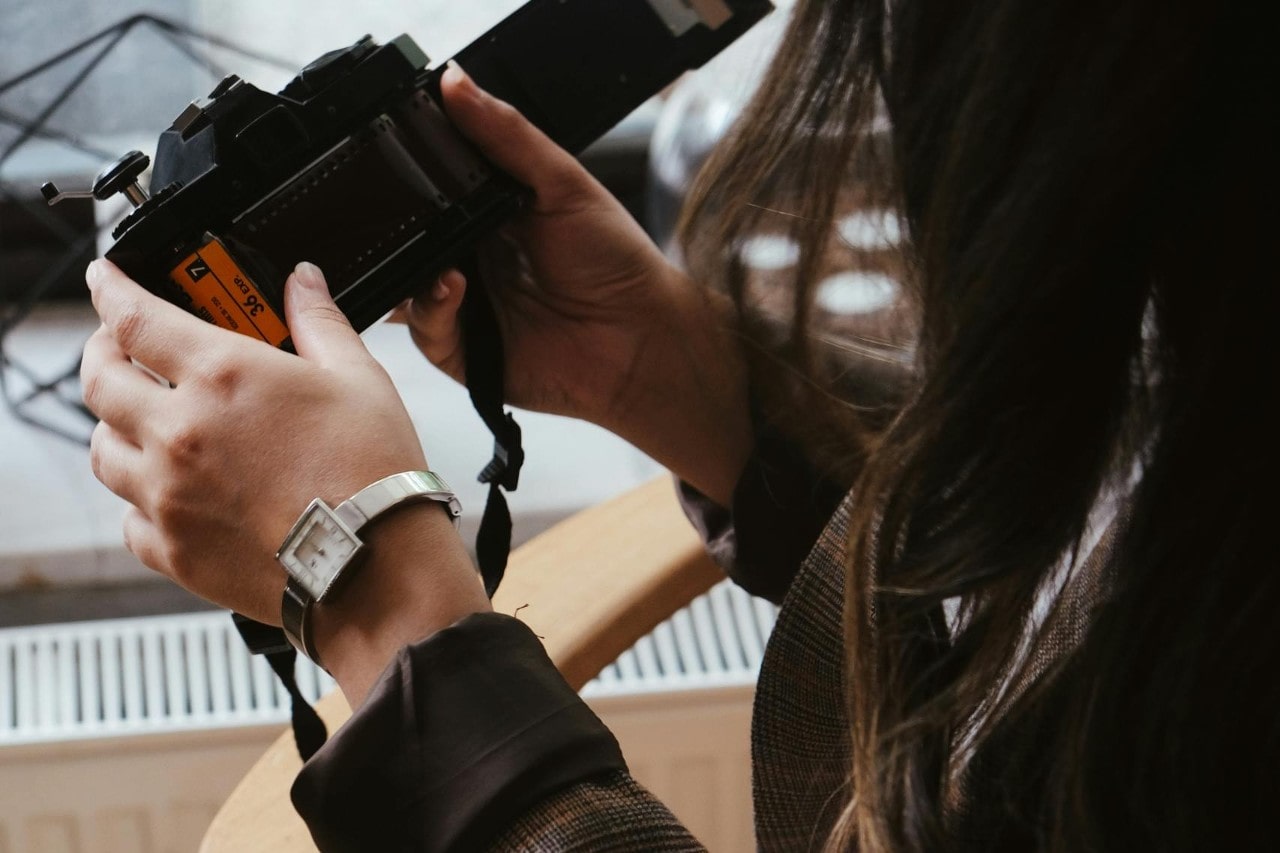 a woman looking into a film camera, wearing a silver watch with a square case