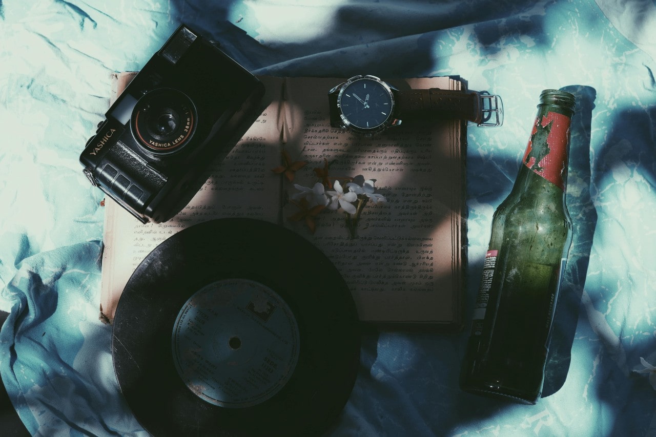 a wrist watch laid out on a book next to a record, camera, and glass bottle