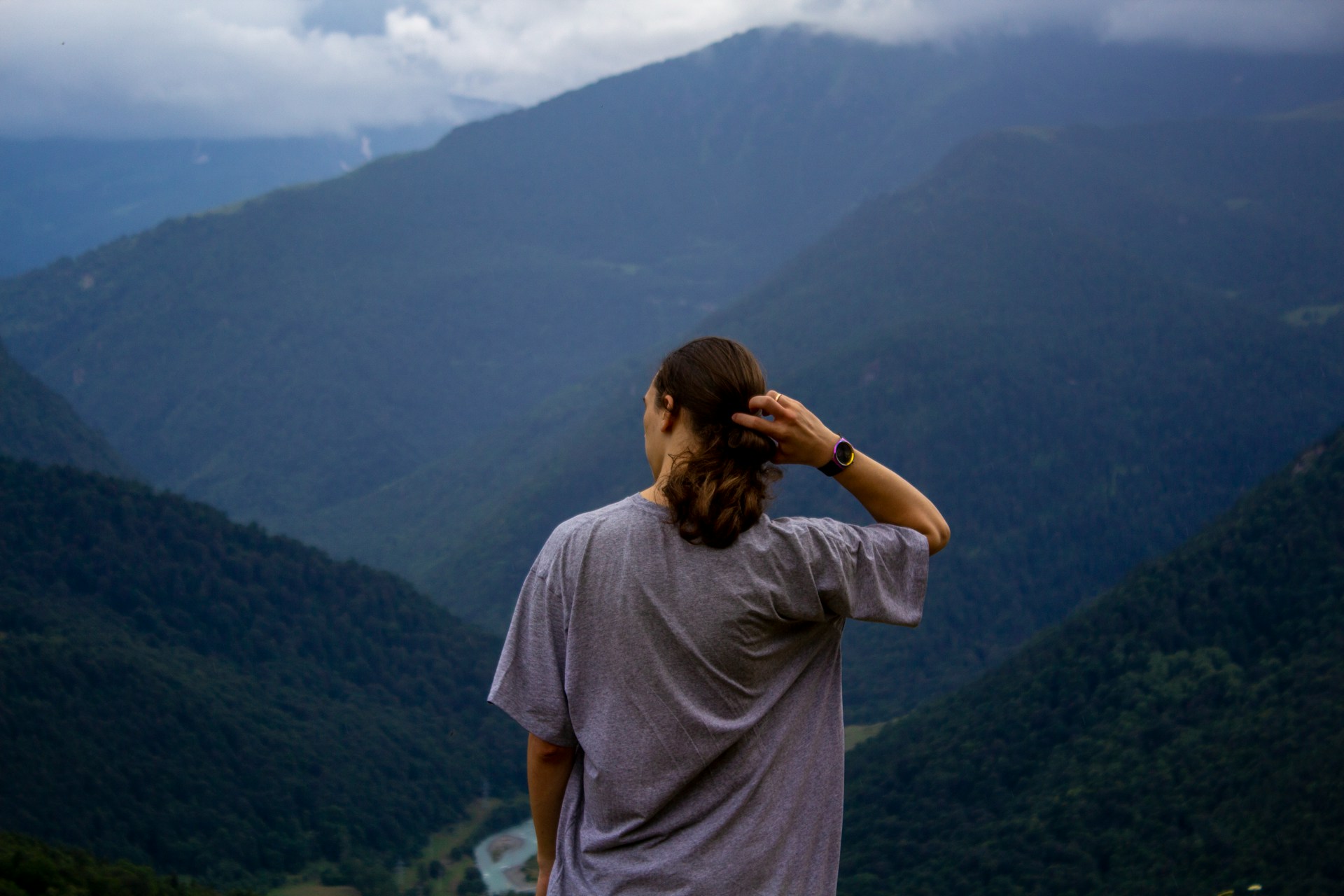 a man standing and looking out over a mountain landscape, wearing a watch on his right wrist.