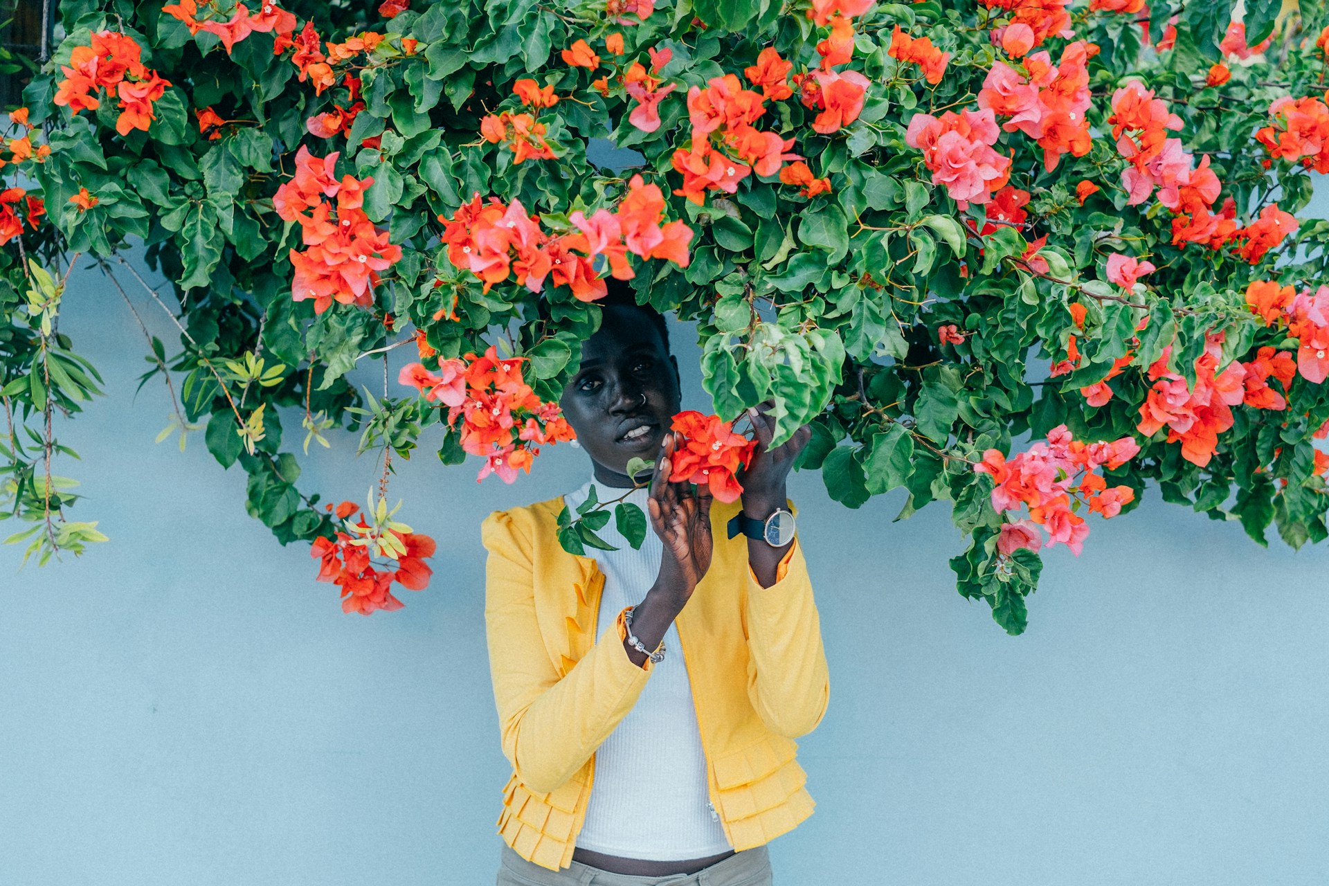 a woman standing under a canopy of flowers, wearing a black and gold watch.