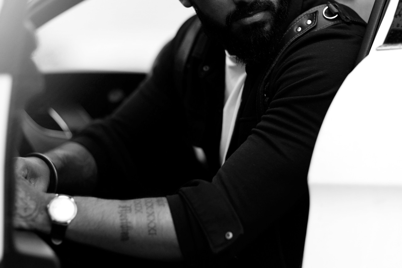 a man leans out of his white sports car, showing off a classic watch with a leather strap.