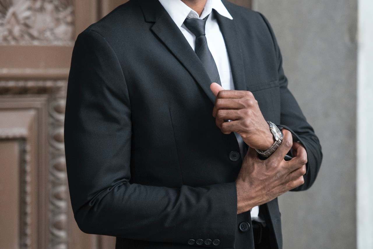 A businessman in a suit adjusts his stainless steel watch from Hamilton.