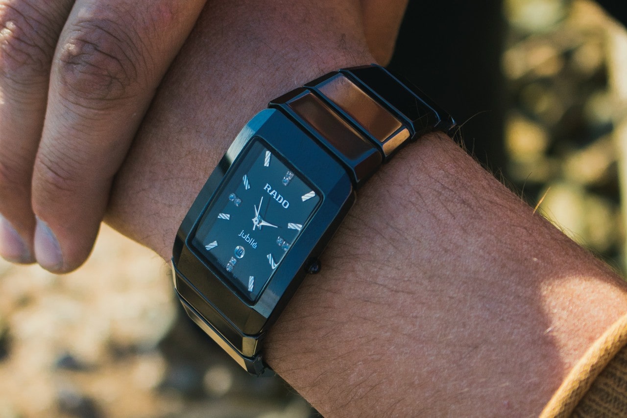 A man checks his rectangular-shaped dial Rado watch while outside.