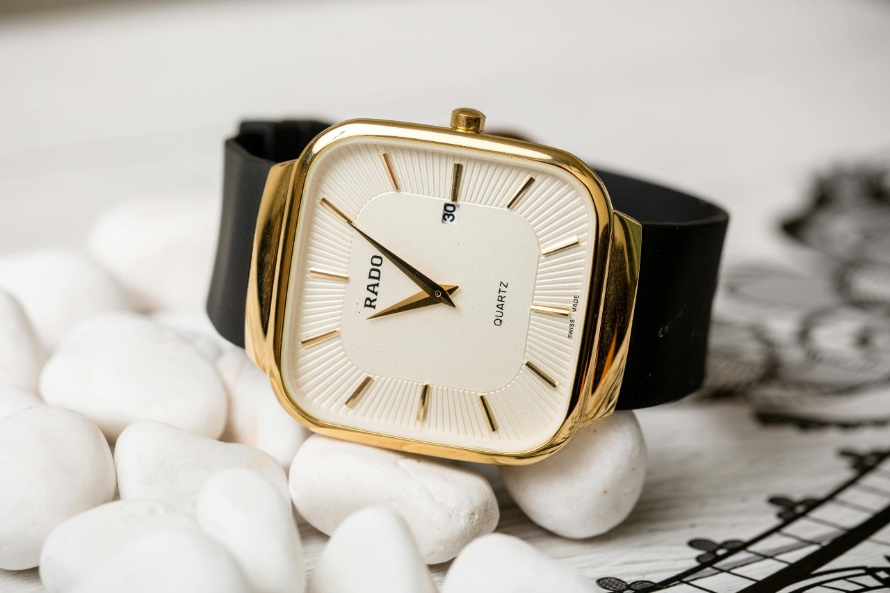 A simple quartz Rado watch sits on a pile of white rocks.