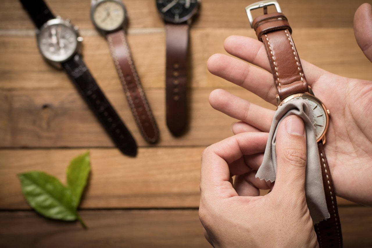A man cleans his collection of leather strap watches with a microfiber towel.