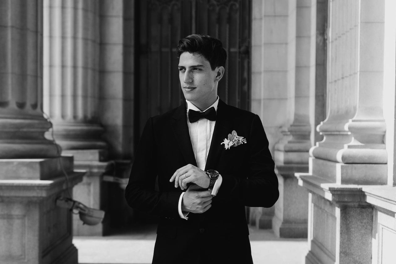 A black and white photo of a young handsome man in a black suit, fixing his metallic wristwatch. A black and white photo of a young handsome man in a black suit, fixing his metallic wristwatch.