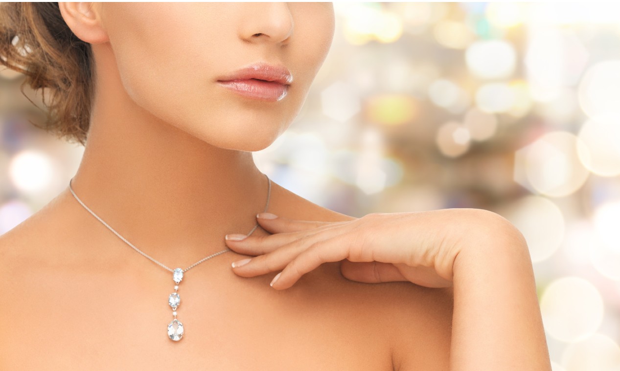 A close-up of a woman wearing a delicate three-stone drop diamond necklace with a soft bokeh background. A close-up of a woman wearing a delicate three-stone drop diamond necklace with a soft bokeh background.