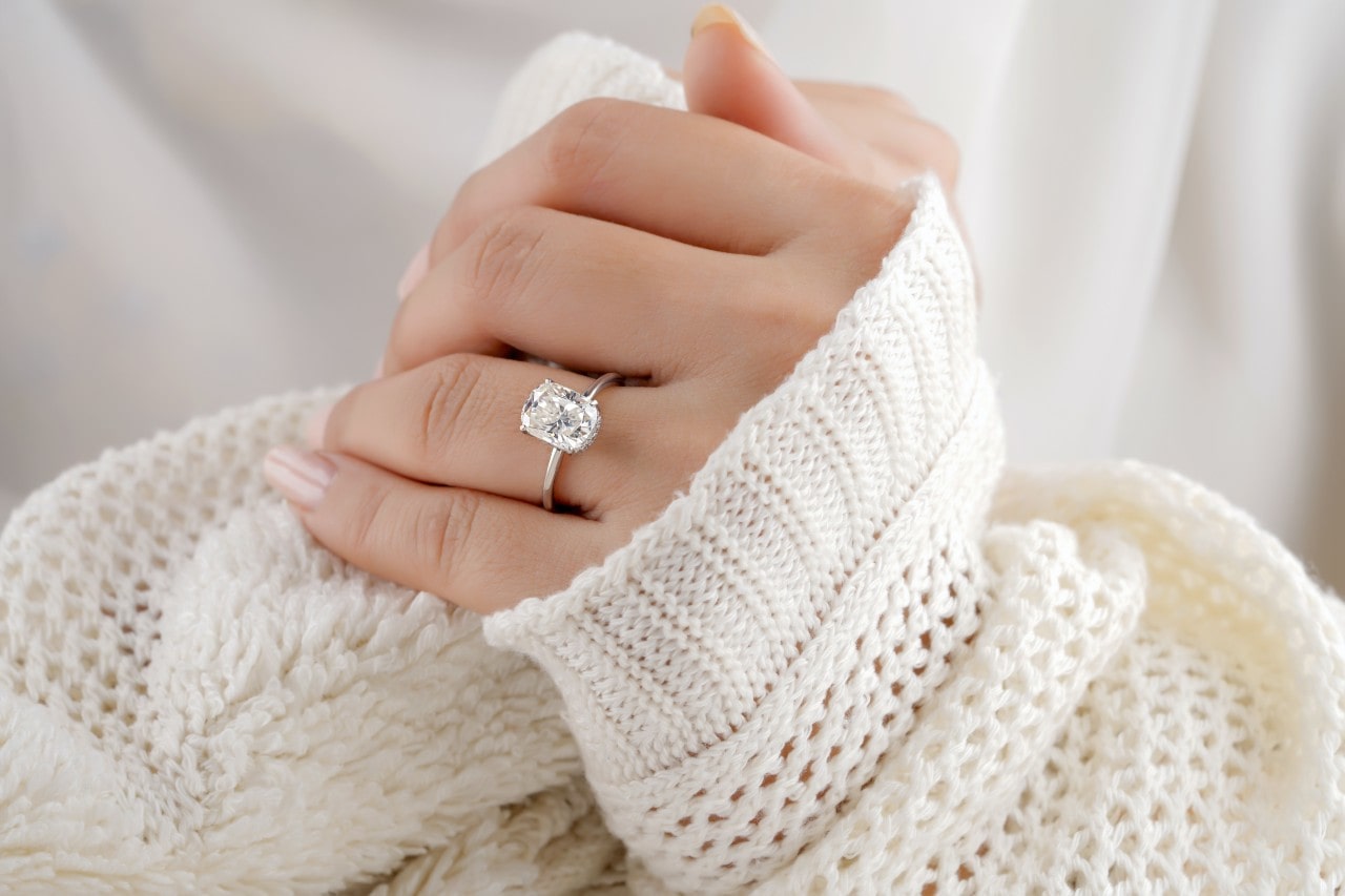 close up of a woman wearing a cream sweater and a solitaire radiant cut engagement ring