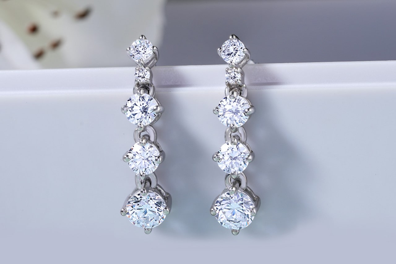 a pair of four-tiered diamond earrings hanging on a white ledge