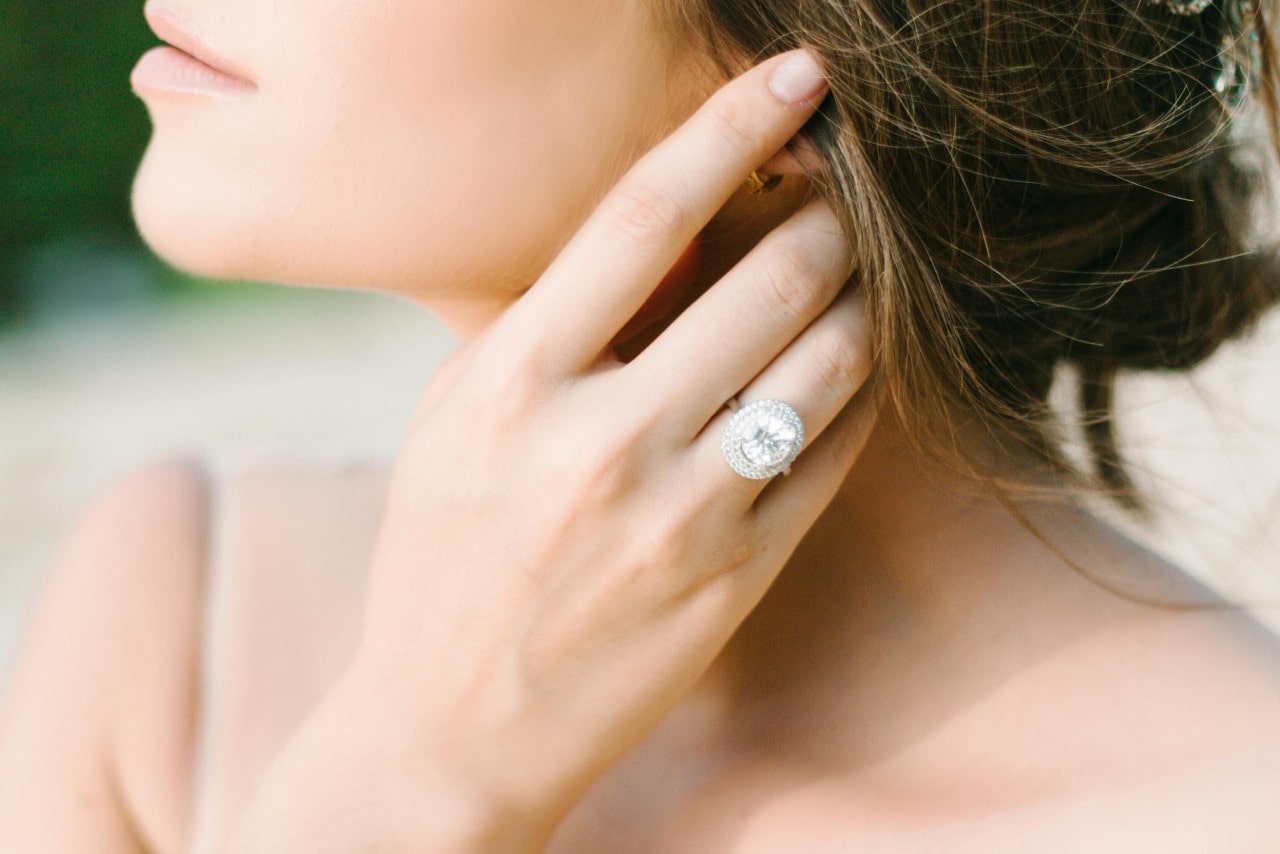 Close-up of a woman gently touching her cheek, showcasing an elegant, sparkling ring on her finger. Her expression is serene and thoughtful. Close-up of a woman gently touching her cheek, showcasing an elegant, sparkling ring on her finger. Her expression is serene and thoughtful.