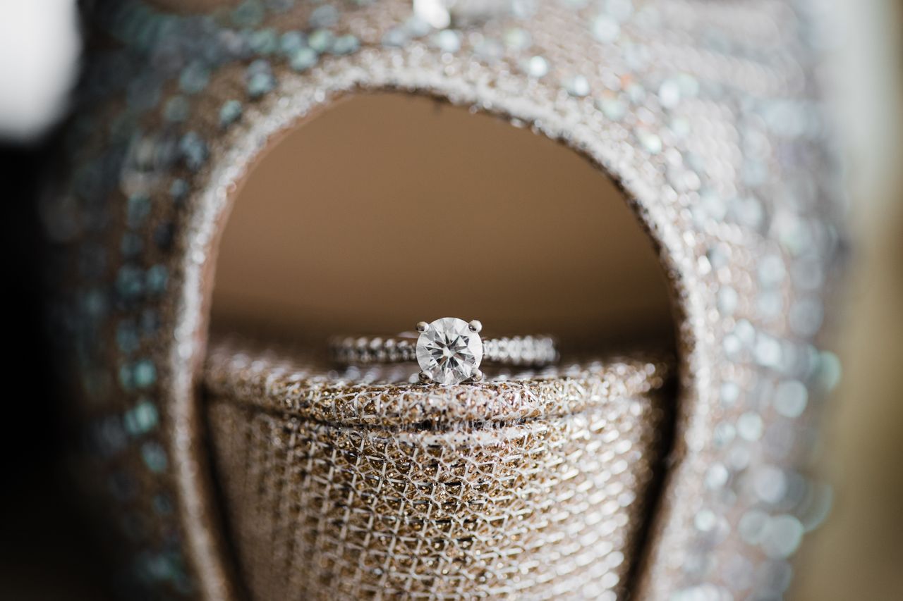 Close-up of a sparkling diamond engagement ring with a round cut stone, set on shimmering fabric with a woven texture, conveying elegance and sophistication. Close-up of a sparkling diamond engagement ring with a round cut stone, set on shimmering fabric with a woven texture, conveying elegance and sophistication.