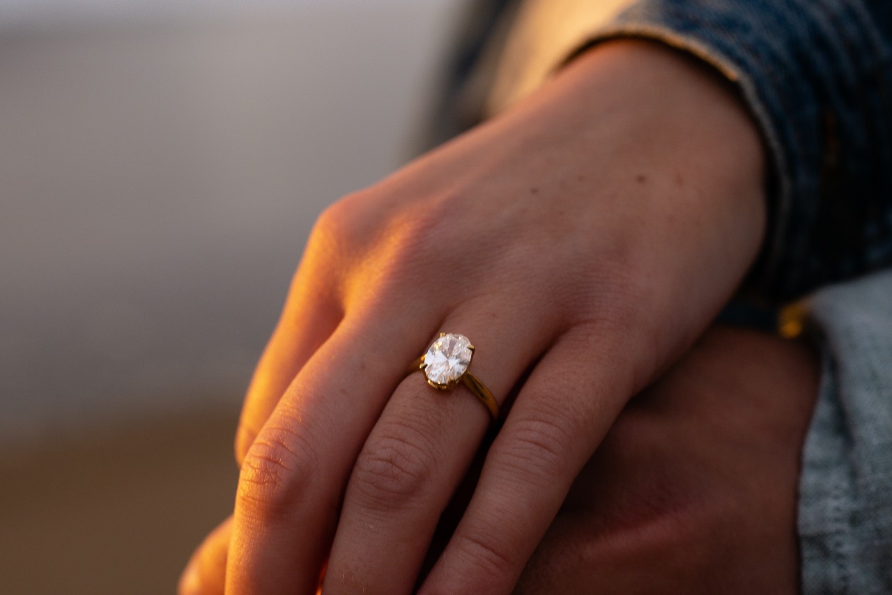 Close-up of a yellow gold oval-cut diamond engagement ring on a woman’s hand in sunset light. Close-up of a yellow gold oval-cut diamond engagement ring on a woman’s hand in sunset light.
