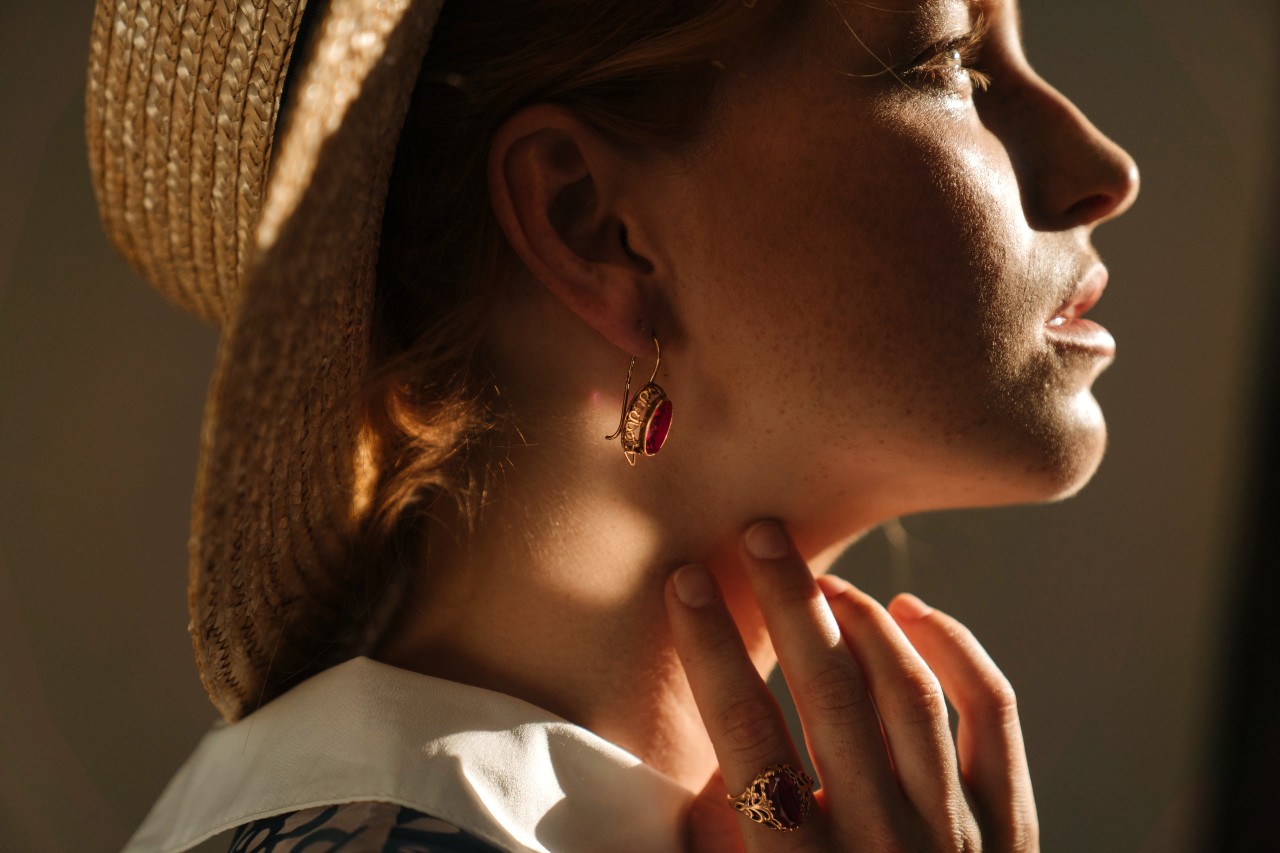 A profile view of a woman in a wicker hat, wearing vintage yellow gold ruby earrings and a matching ring.