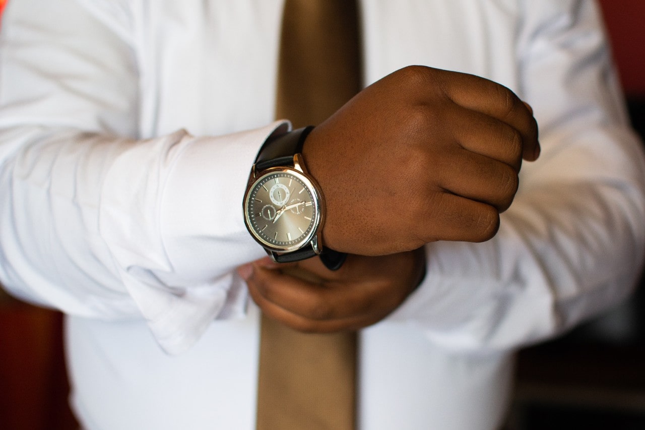 Man in a white shirt and a tie putting on a gold and brown watch with a leather strap