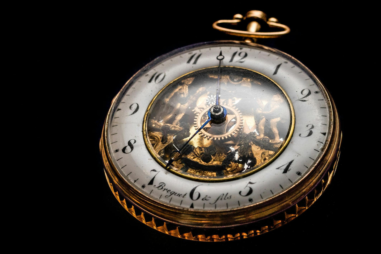 A close-up of a vintage Breguet pocket watch with a skeleton dial on a black background.