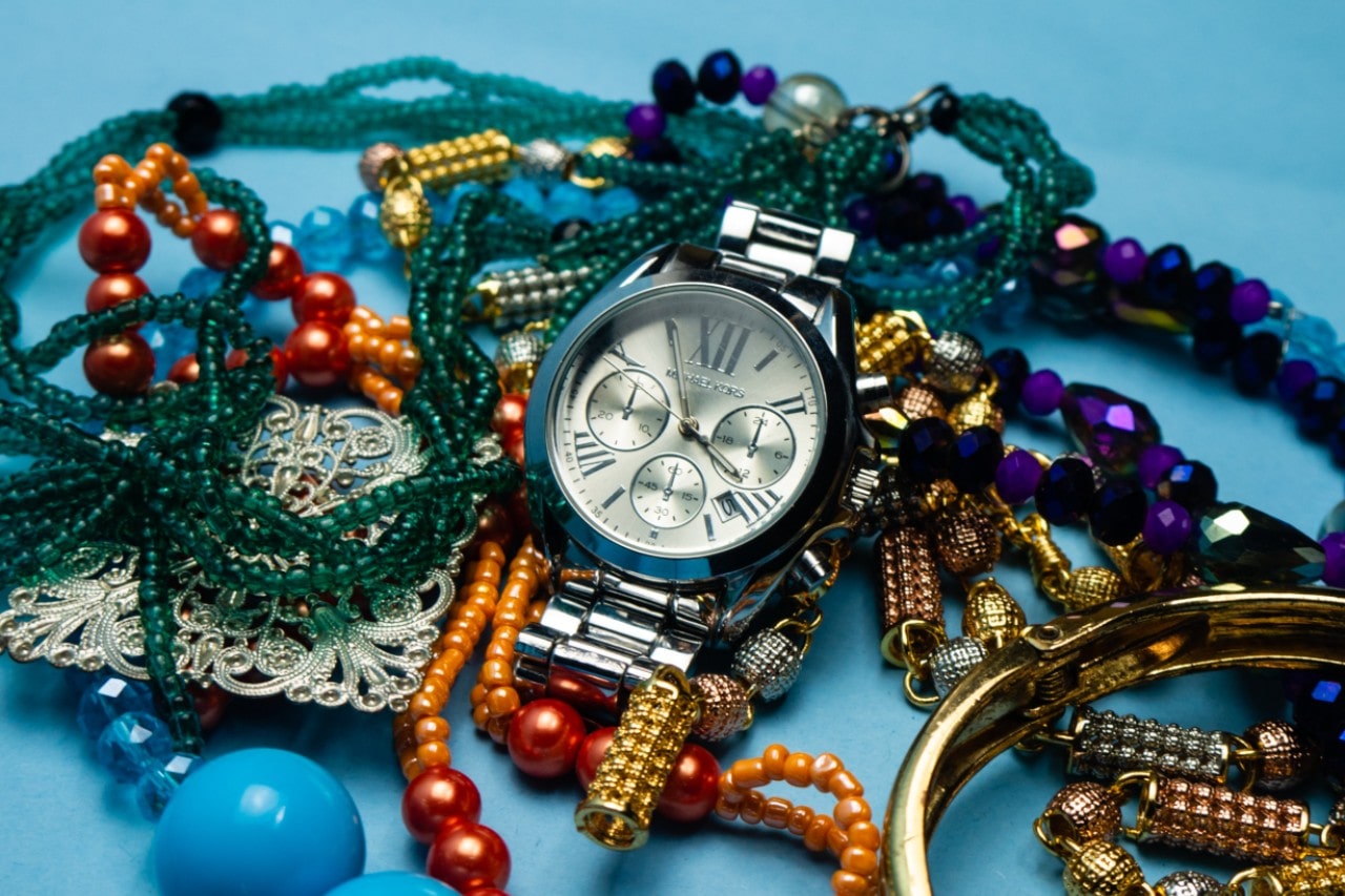 A silver watch lying on a bed of brightly colored, beaded jewelry against a blue background