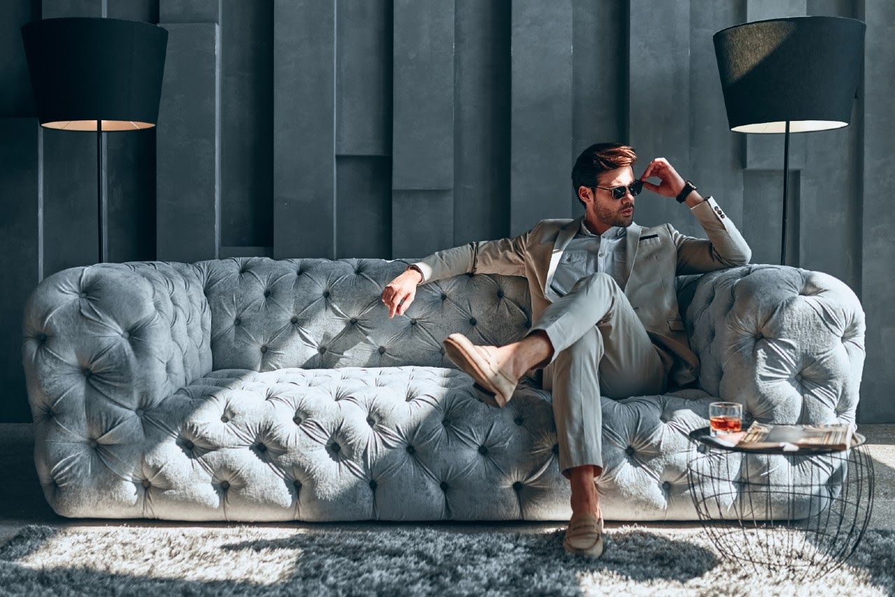 A man in a suit lounges on a luxurious gray couch