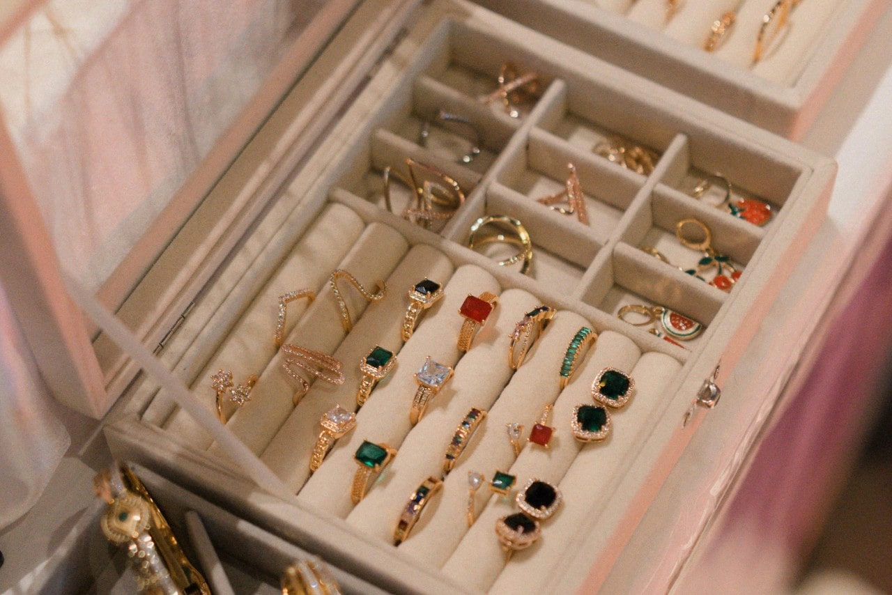 A view of an open jewelry box displaying a neatly organized array of gold rings with colorful center stones.