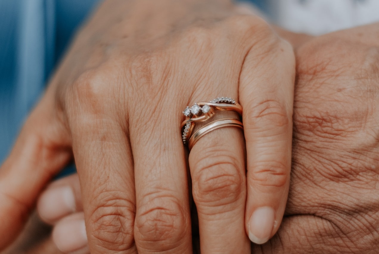 A close up of a rose gold bridal stack with polished wedding band and intertwined diamond engagement ring on a finger.