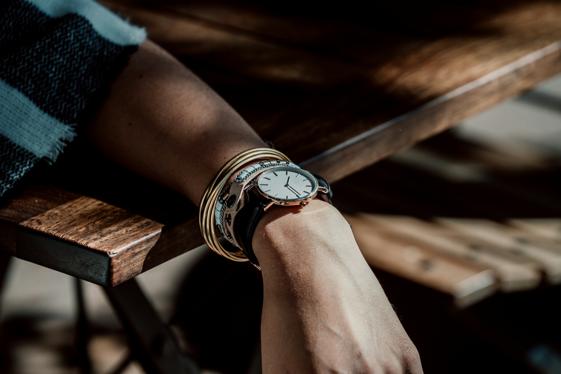 an arm resting on a wood table wearing a fine watch