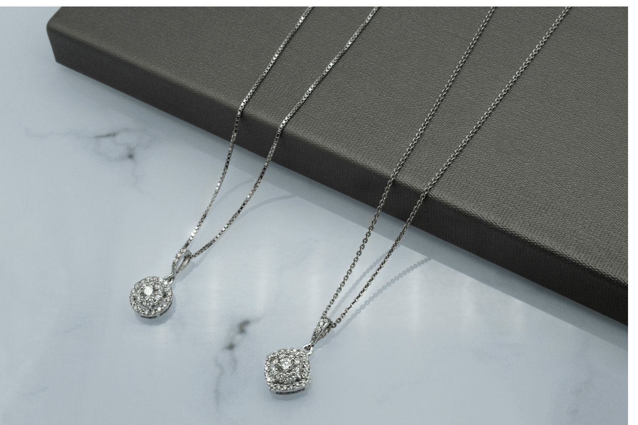 A close-up of two delicate diamond pendant necklaces displayed side-by-side on a marble counter.