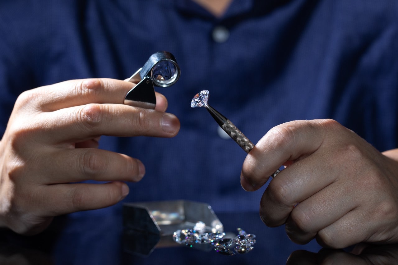 A close-up of a jeweler examining a round cut diamond under a magnifying lens.