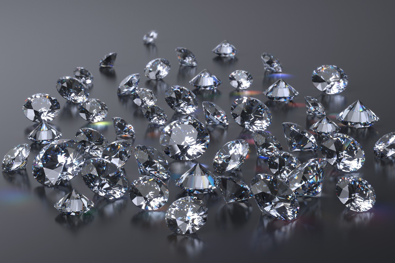 Numerous round brilliant-cut diamonds are scattered across a reflective dark surface, creating rainbow reflections.