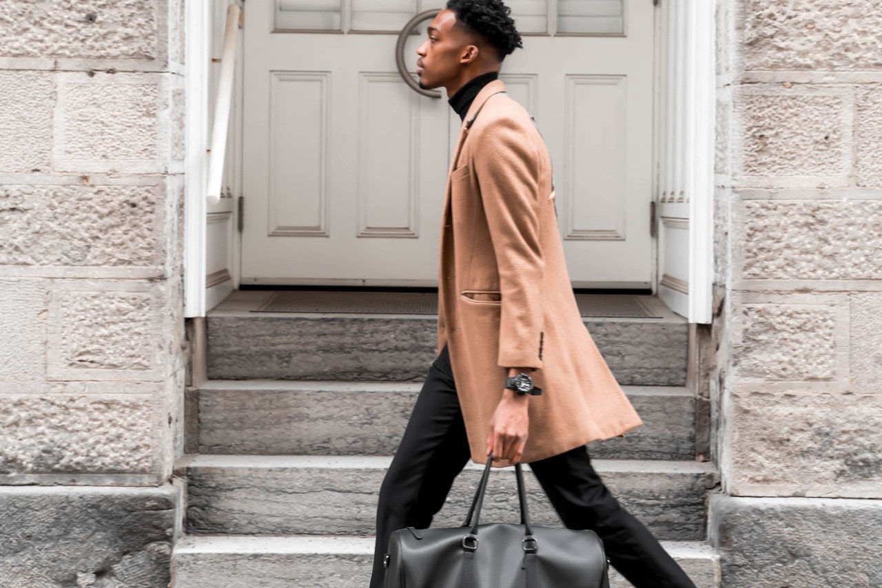 man walking down the street holding a black bag and wearing a black watch