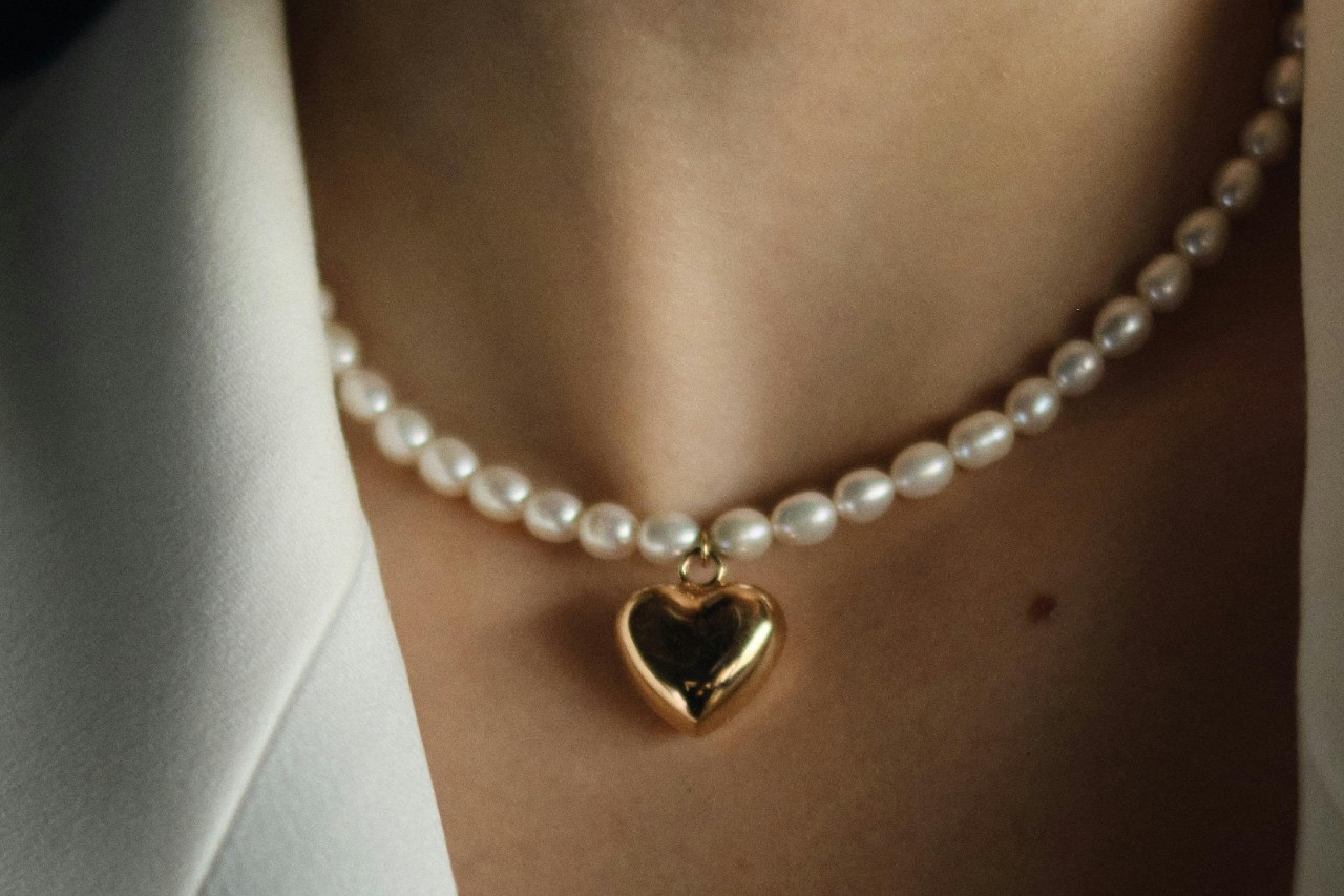 A close-up image of a woman wearing a pearl and heart pendant necklace. A close-up image of a woman wearing a pearl and heart pendant necklace.