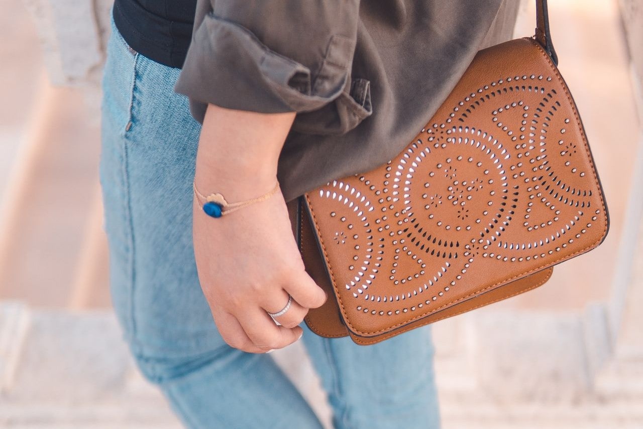 a woman walking and wearing a brown bag and two gold chain bracelets, one with a blue gemstone