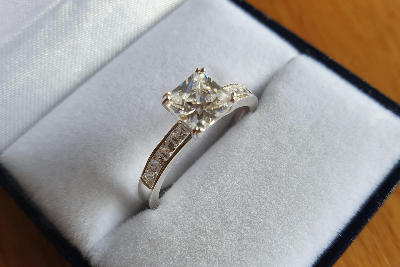 A close-up of a vintage style ring with a princess cut diamond in a white and blue velvet ring box.