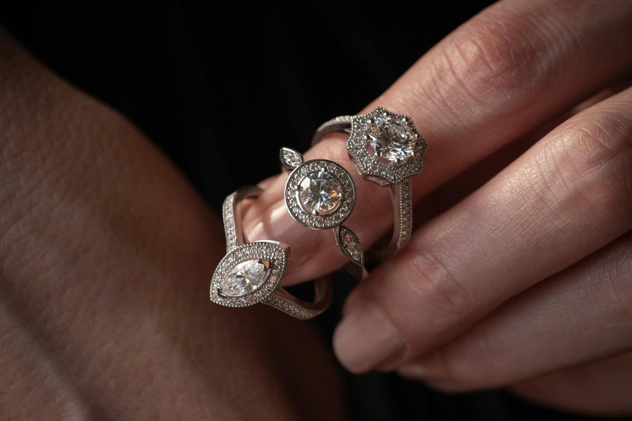 A manicured hand with three engagement rings looped around one finger, all different diamond shapes.