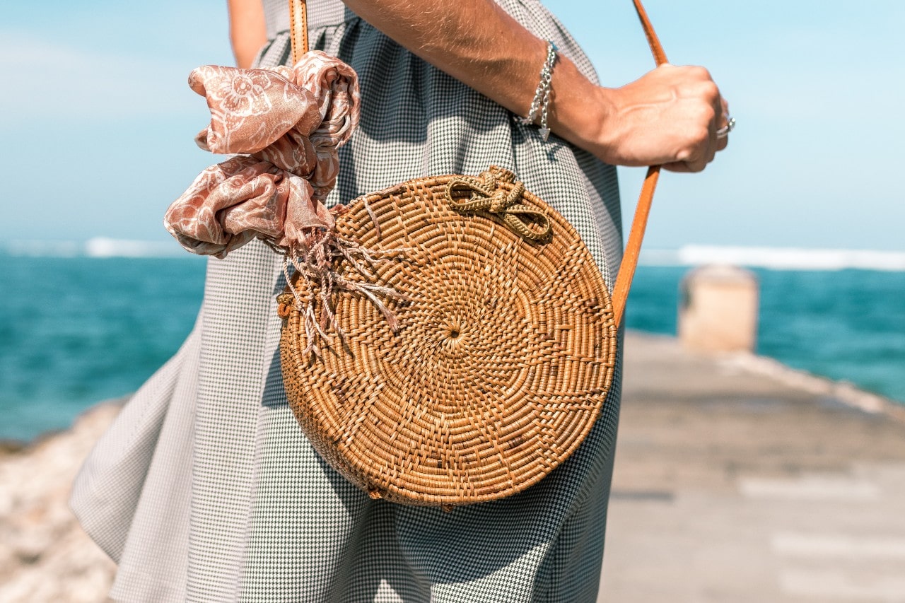 A woman at the beach holds her bag while wearing a bracelet.