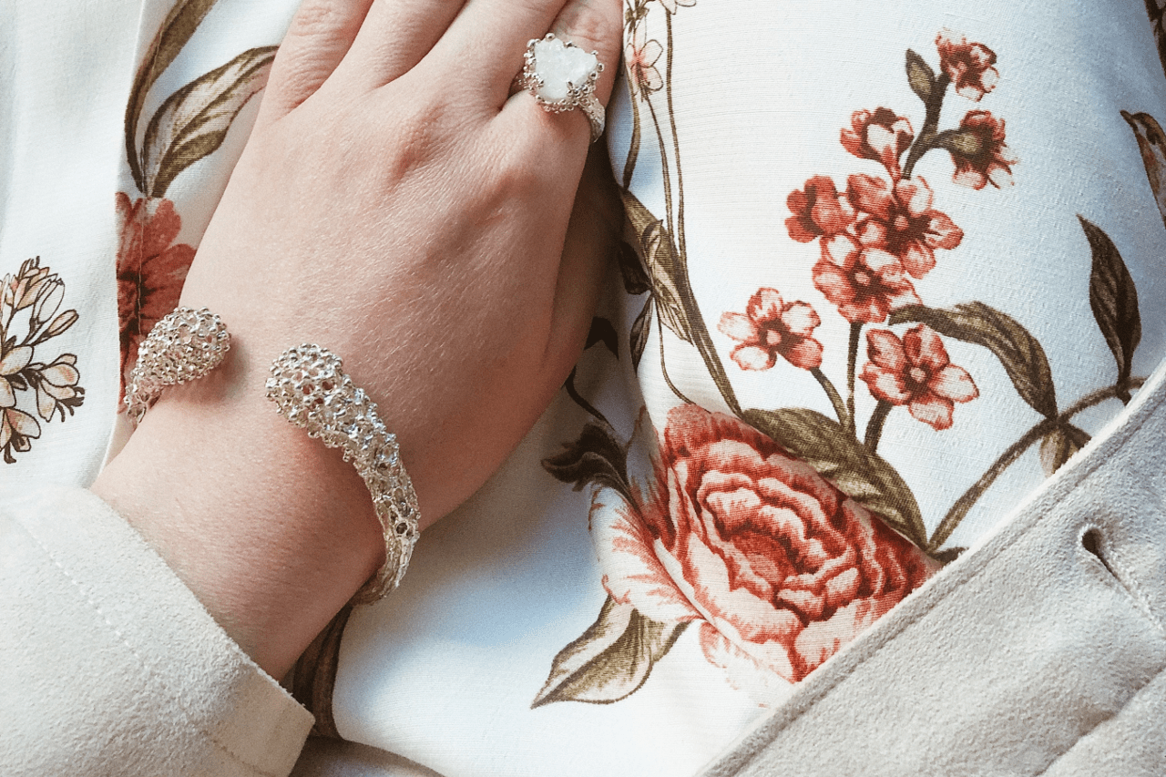 A woman wearing a cuff bracelet rests her hand on her chest.