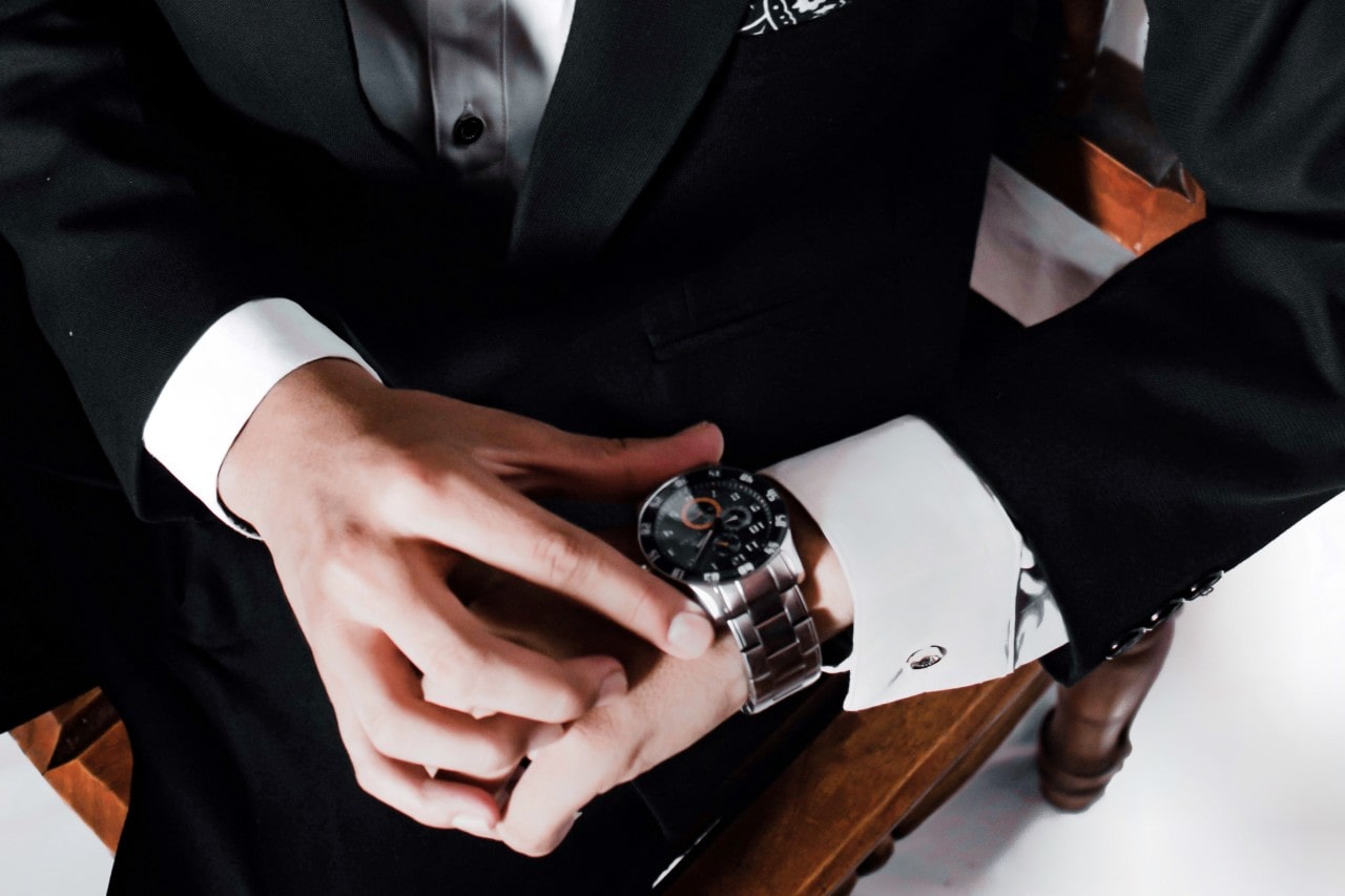 A in a suit adjusting a silver and black watch on his wrist
