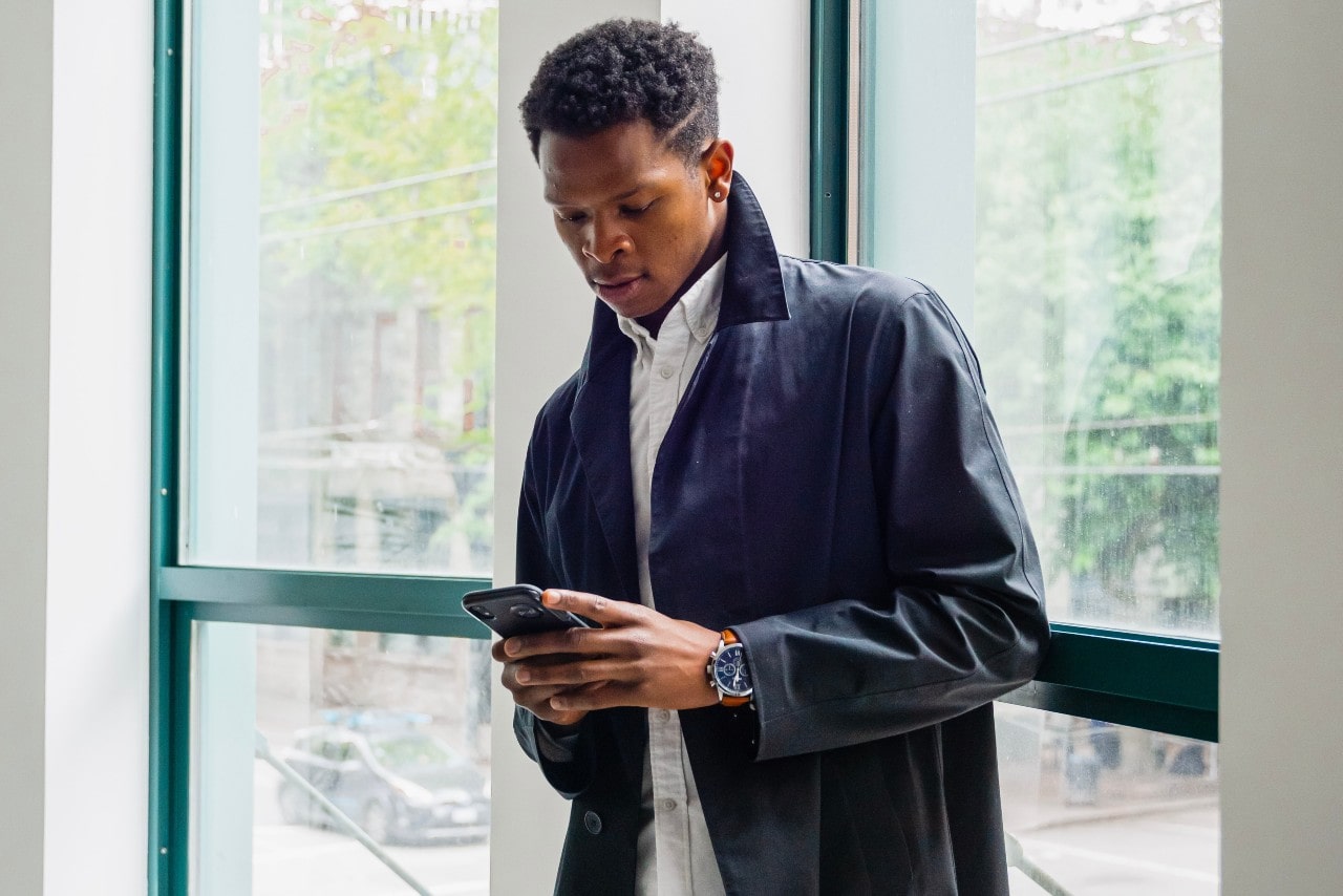 A man in a black coat looking at his phone and wearing a silver and black watch