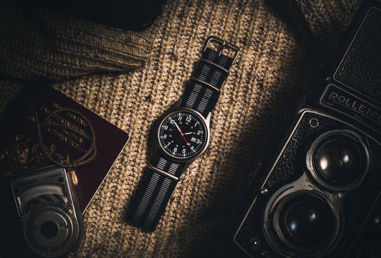 A black watch sitting amongst black, vintage items on a woven surface